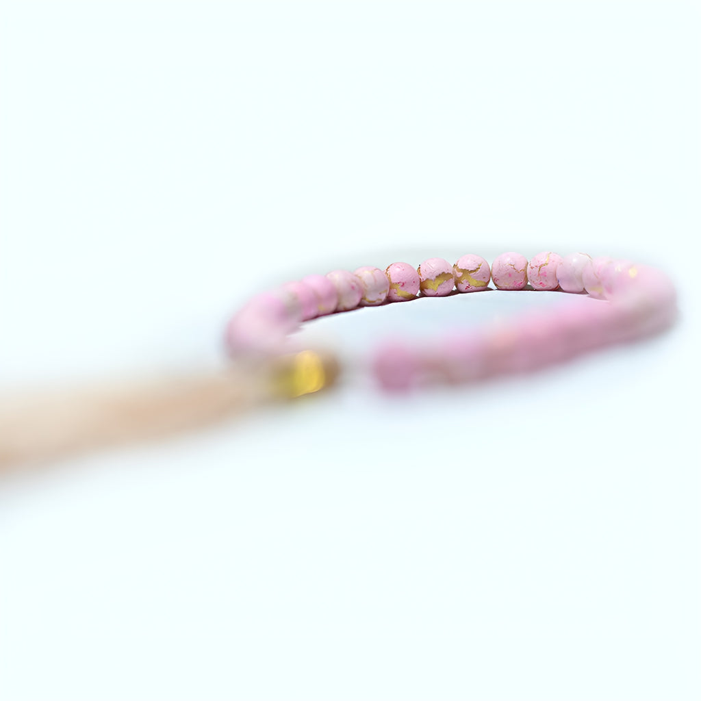 Pink pearl prayer beads from Zamzam Zarqun LLC displayed on a prayer mat with intricate patterns.