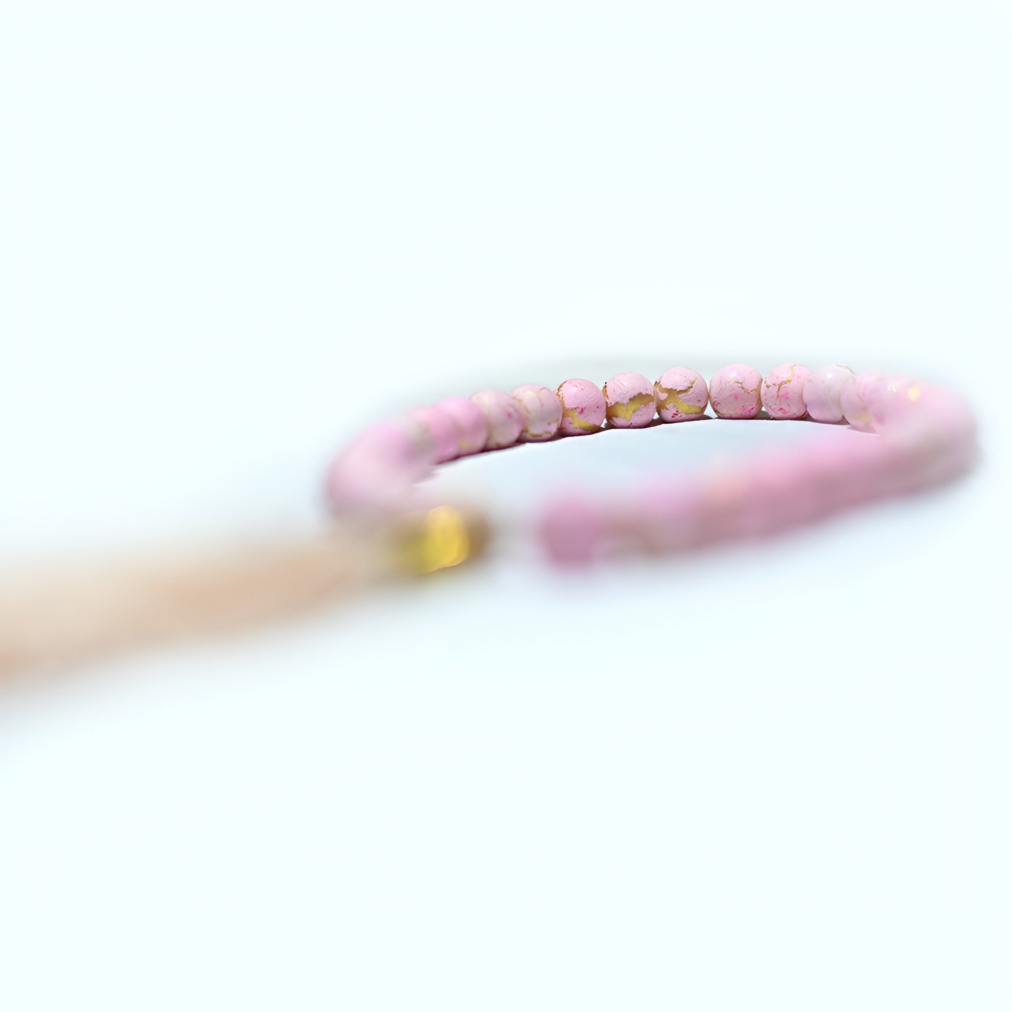 Pink pearl prayer beads from Zamzam Zarqun LLC displayed on a prayer mat with intricate patterns.